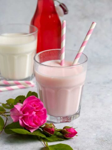 Table with a glass of milk, rose syrup and a glass of rose milk.