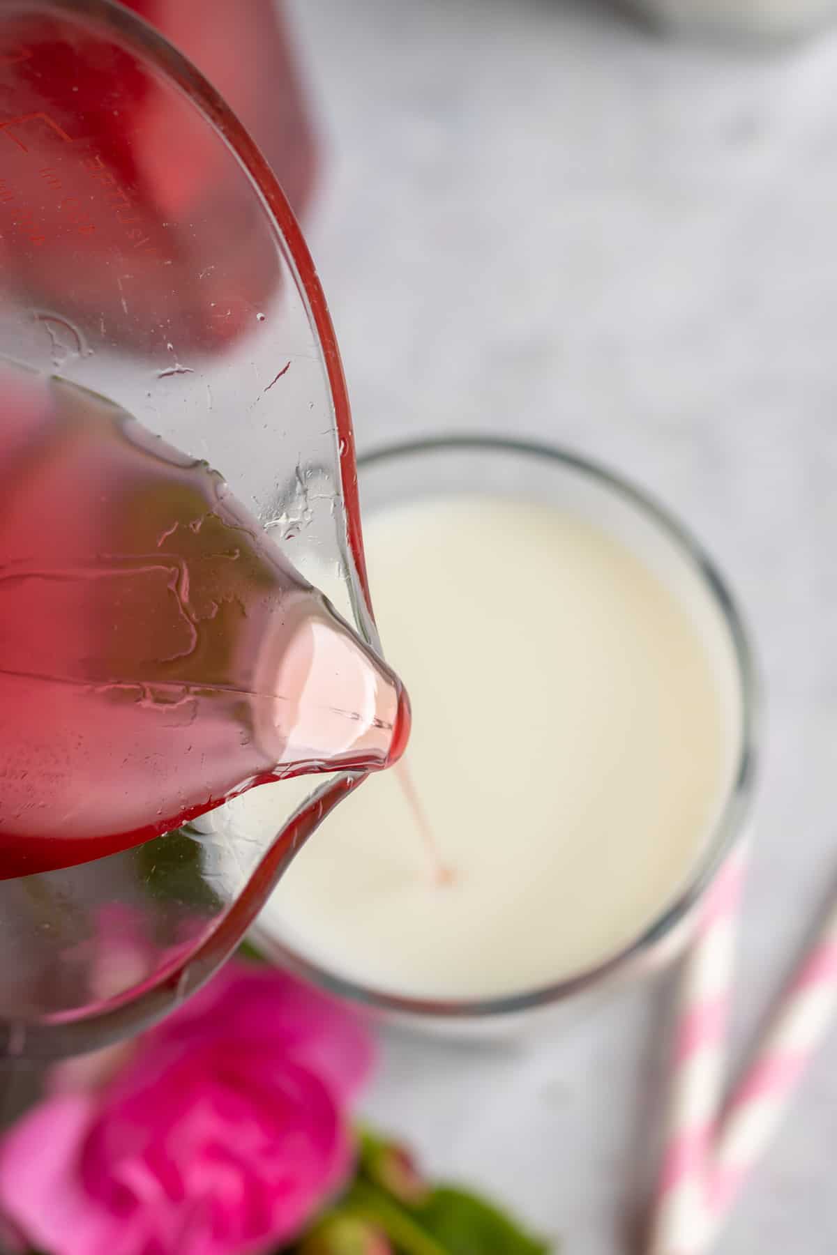 Pouring rose simple syrup into a glass of milk.