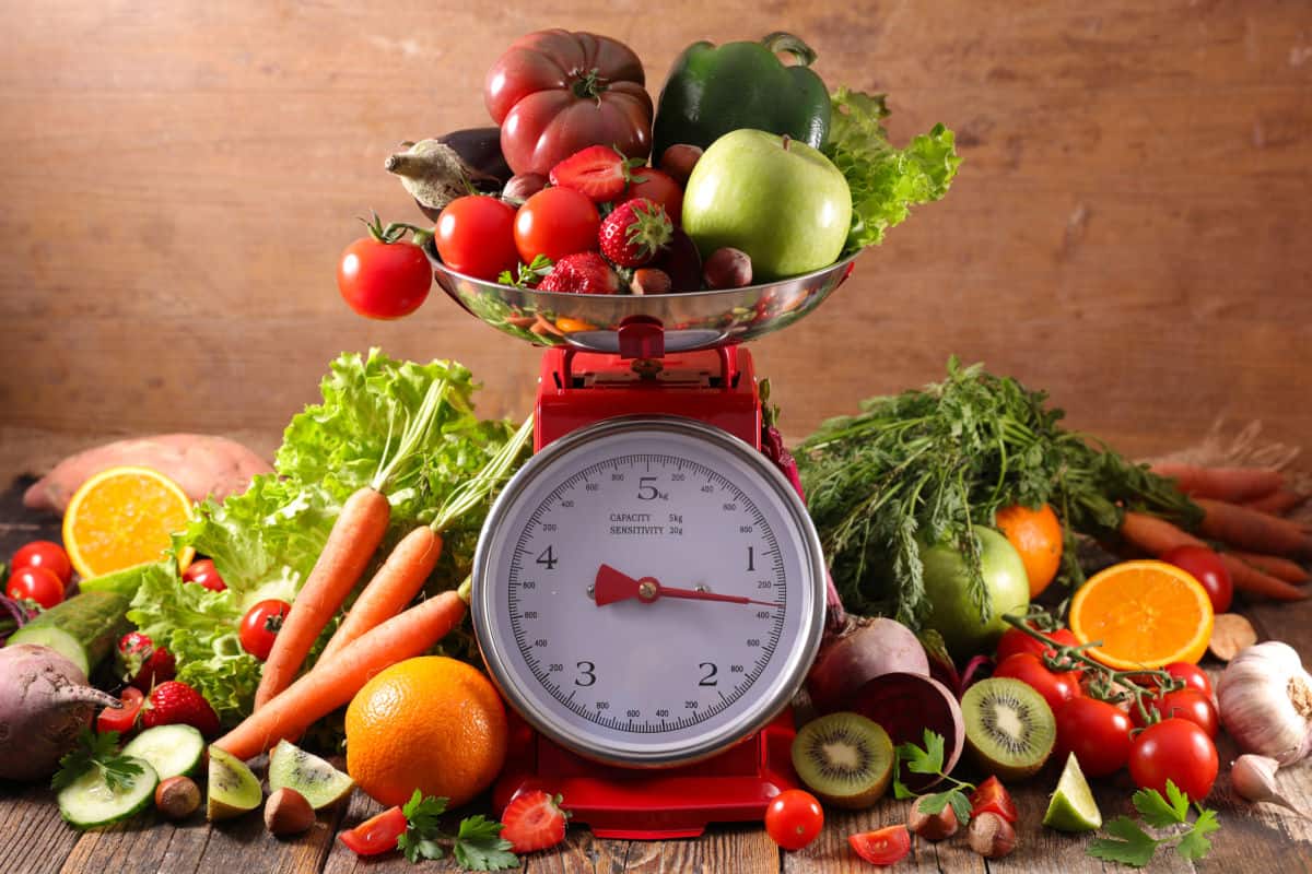 Kitchen scale surrounded by fruit and vegetables..