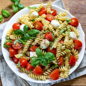 Wooden table with a serving dish of caprese pasta salad.