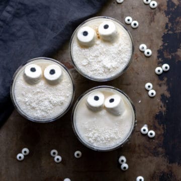 Three glasses of halloween smoothie topped with marshmallow eyes.