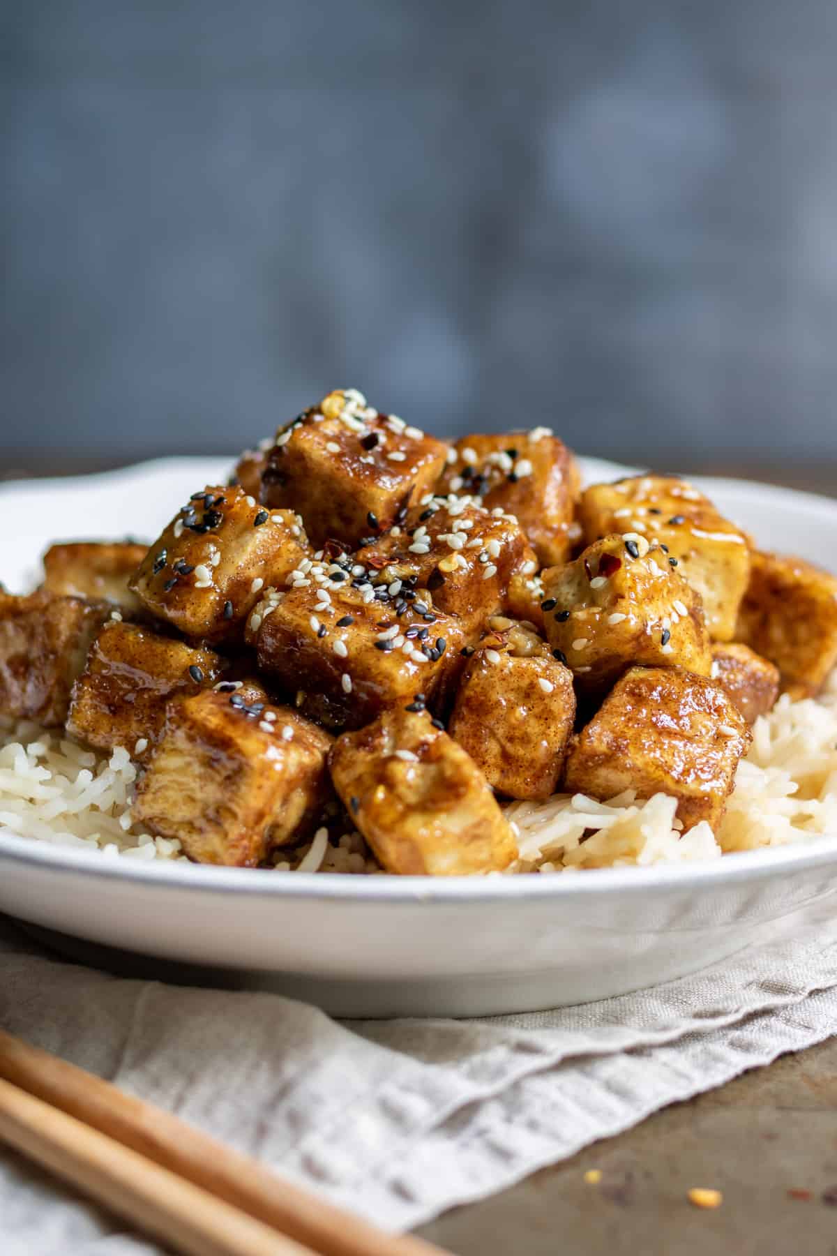 A plate of rice topped with sticky tofu and sesame seeds.