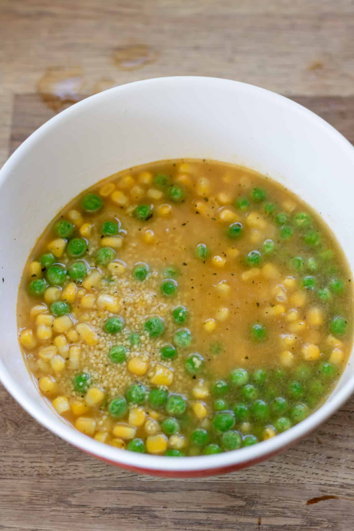 Couscous, frozen peas and corn and vegetable stock in a bowl.