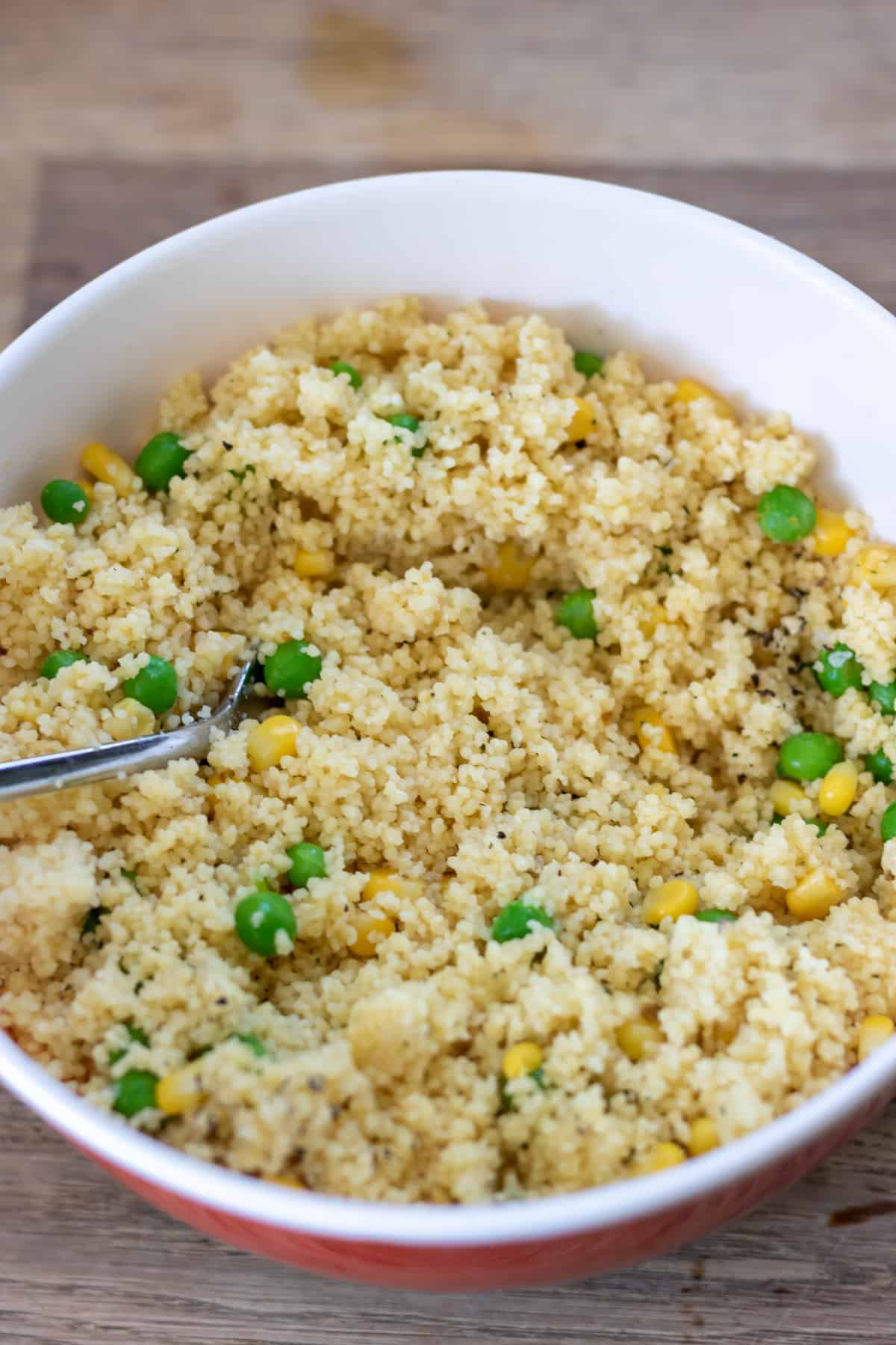 Bowl of cooked couscous with peas and corn.