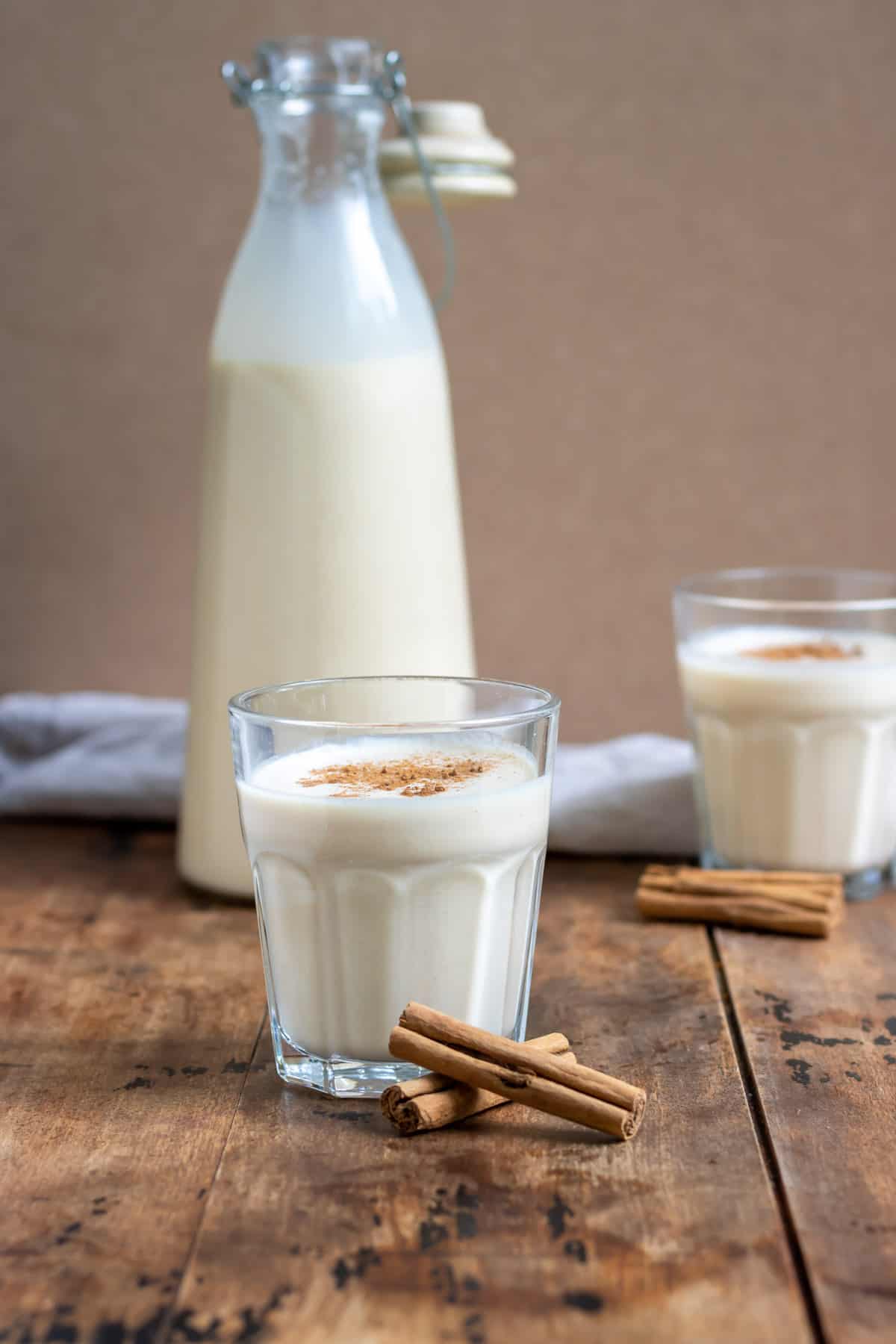 Glasses of coquito in front of a bottle of it.