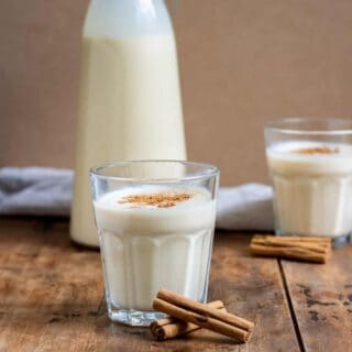 Glasses of coquito in front of a bottle of it.