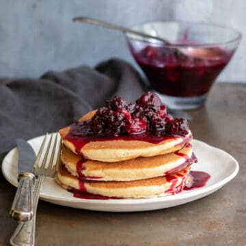 A table with a plate of pancakes topped with frozen berry compote.