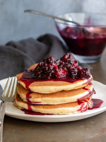 A table with a plate of pancakes topped with frozen berry compote.