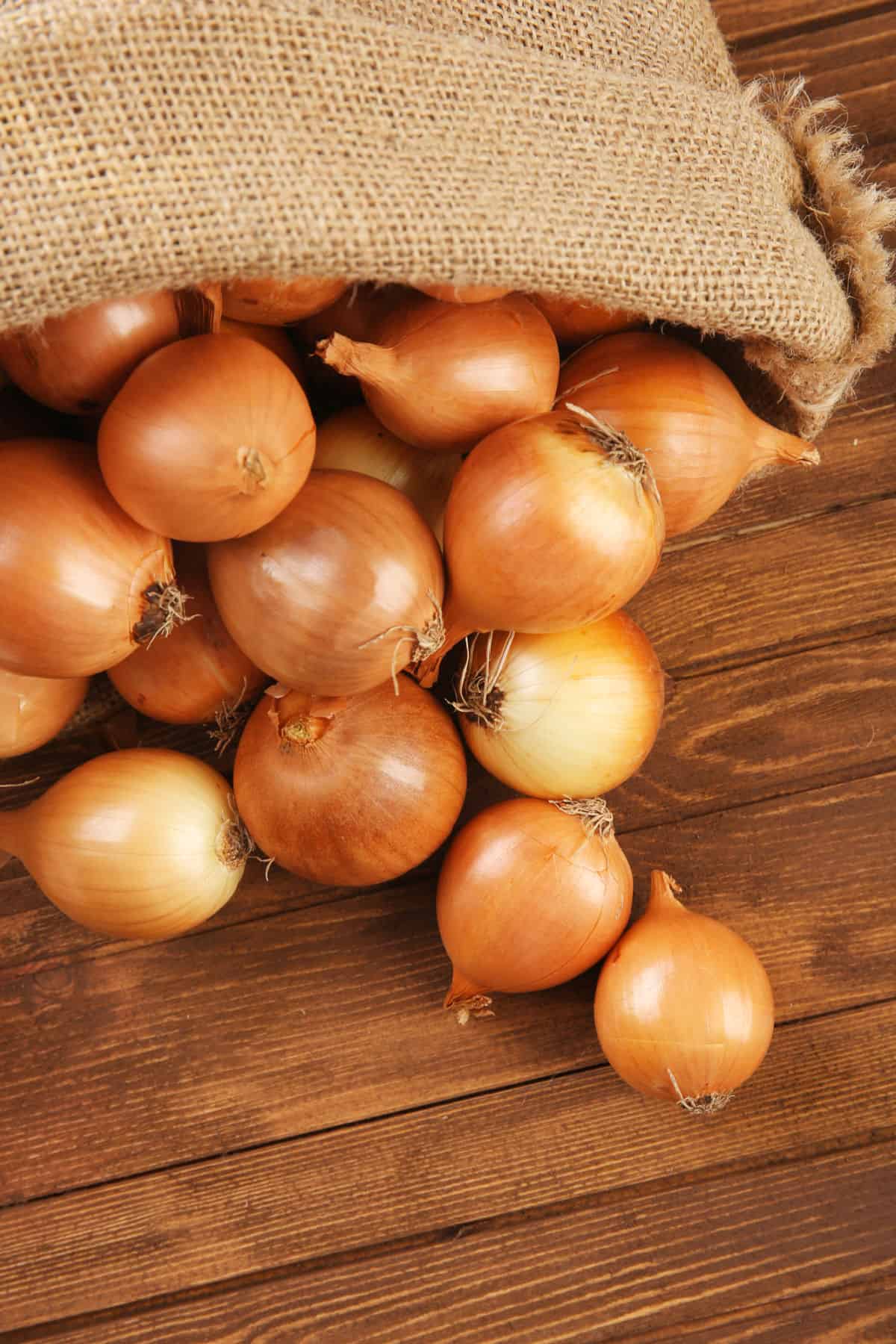 A bag with onions spilling out onto a wooden table.