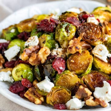 Plate of roasted brussels sprouts topped with goat cheese, walnuts and cranberries.
