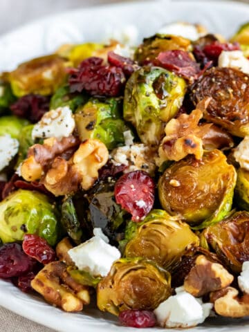 Plate of roasted brussels sprouts topped with goat cheese, walnuts and cranberries.  Apple Parsnip Cupcakes with Boozy Apple Ci brussels sprouts goat cheese walnuts sq 360x480