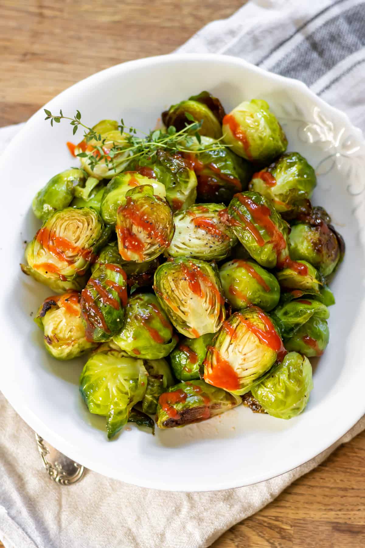 Wooden table with a bowl of roasted honey sriracha brussels sprouts.
