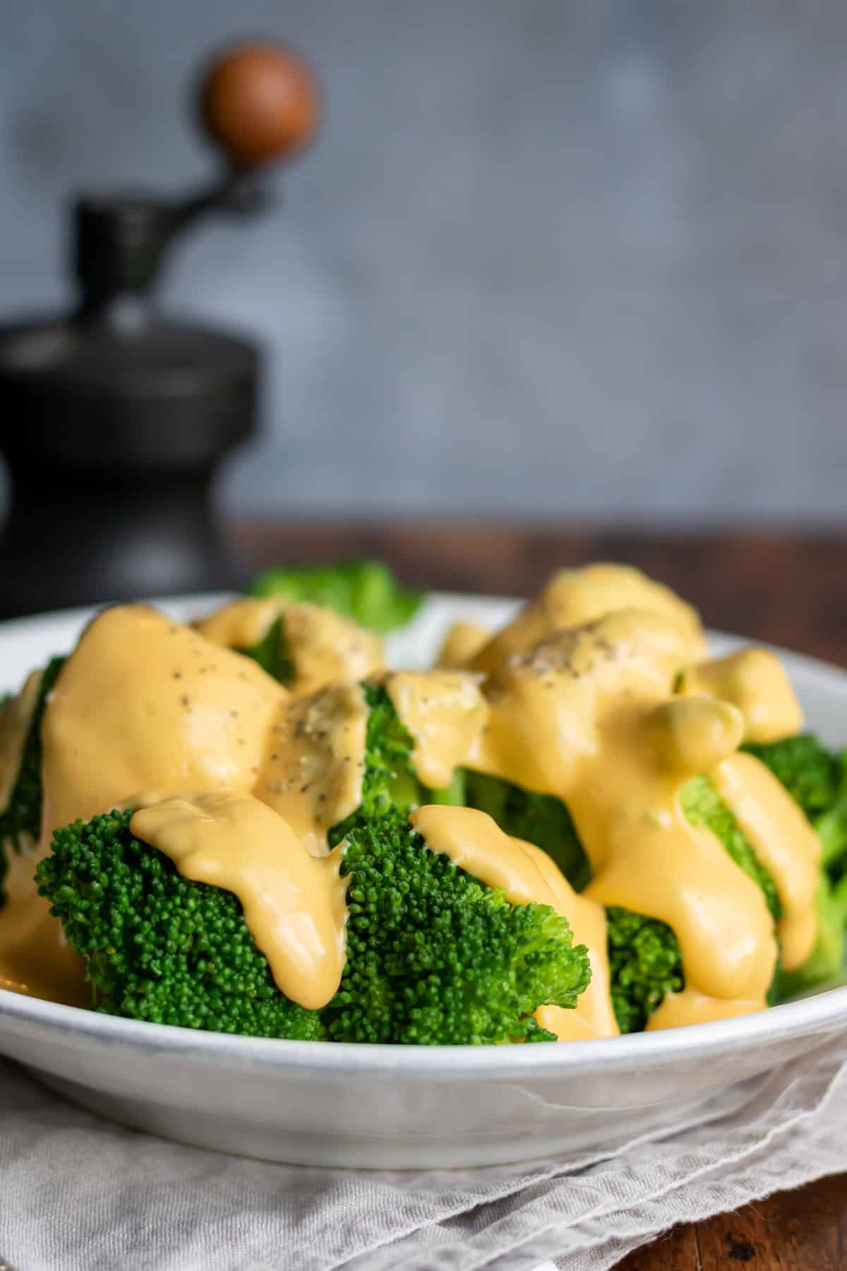Table with a serving dish of broccoli with cheese sauce.