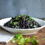 Wooden table with a bowl piled with black beans made in a slow cooker.
