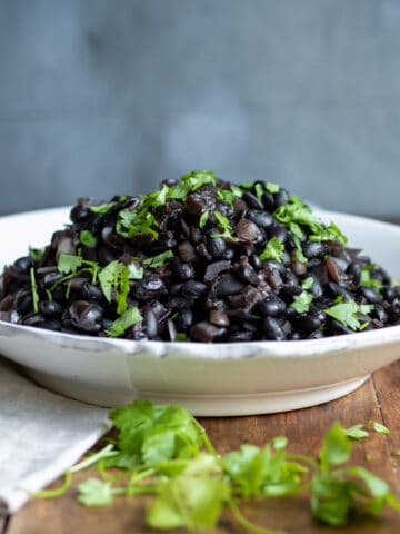 Wooden table with a bowl piled with black beans made in a slow cooker.