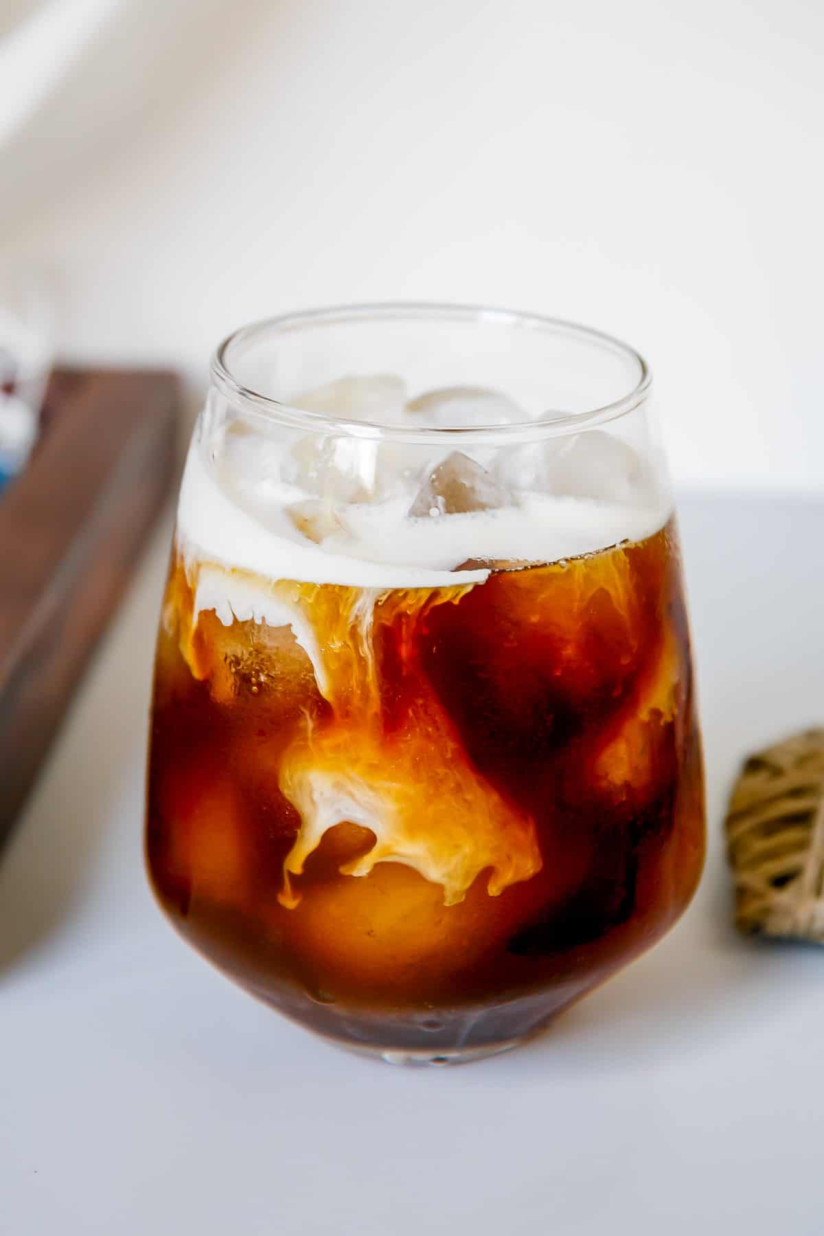 Side view of cold foam swirling into a glass of caramel cold brew coffee.