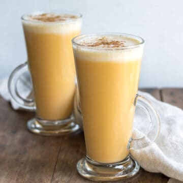 Two glasses of frothy sweet potato latte on a wooden table.