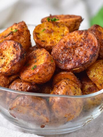 Glass bowl full of air fryer roasted potatoes, on a table.