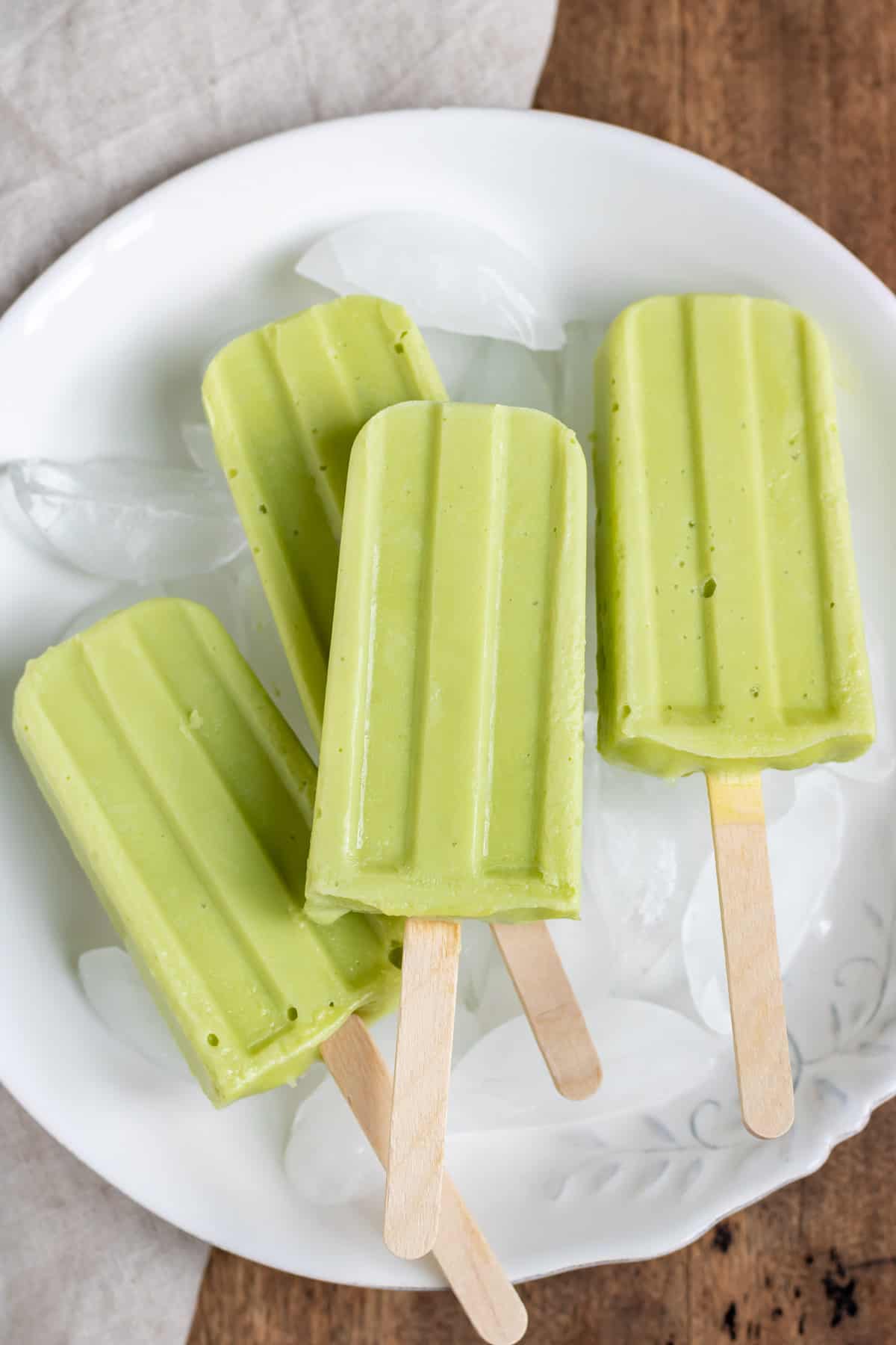 Table with a bowl of ice and lime avocado popsicles.