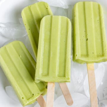 Pile of lime avocado popsicles on a bowl of ice.