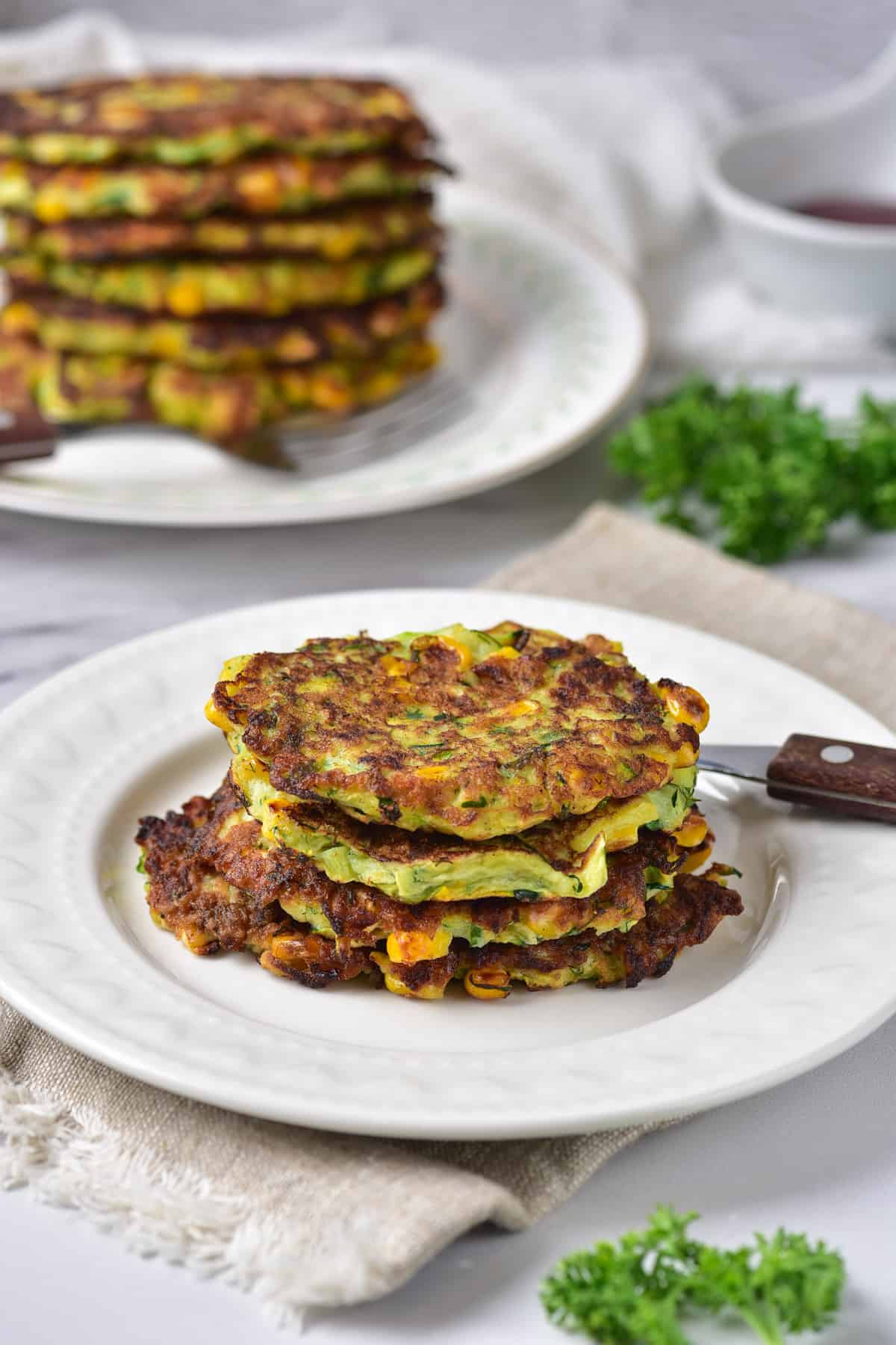 Side view of a plate with a stack of three zucchini and corn fritters.