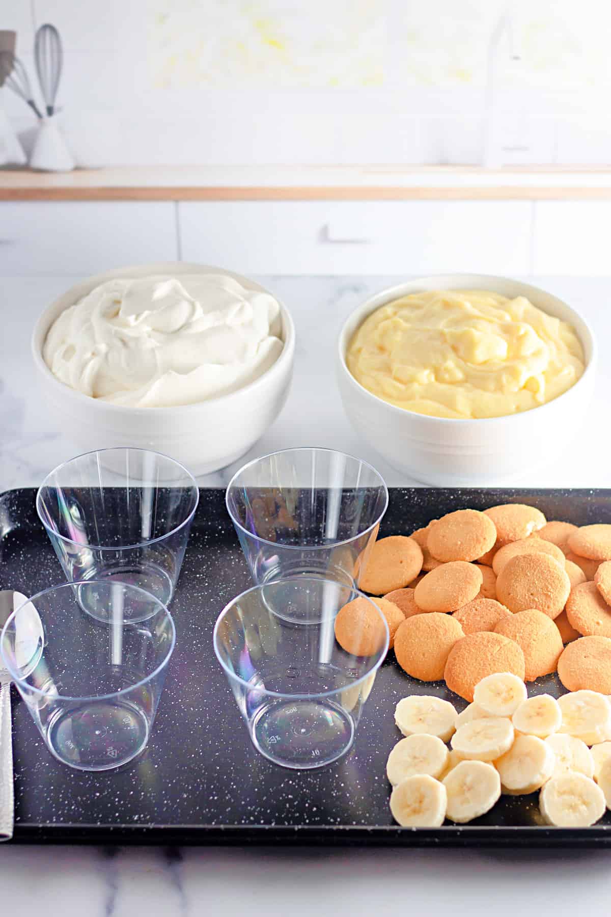 Tray of cups, sliced banana, nilla wafers, plus bowls of whipped cream and vanilla pudding.