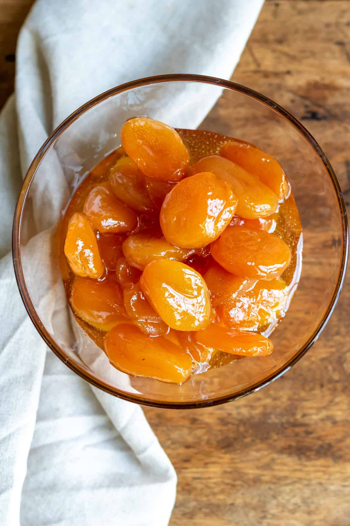 Wooden table with a glass bowl of glazed apricots.