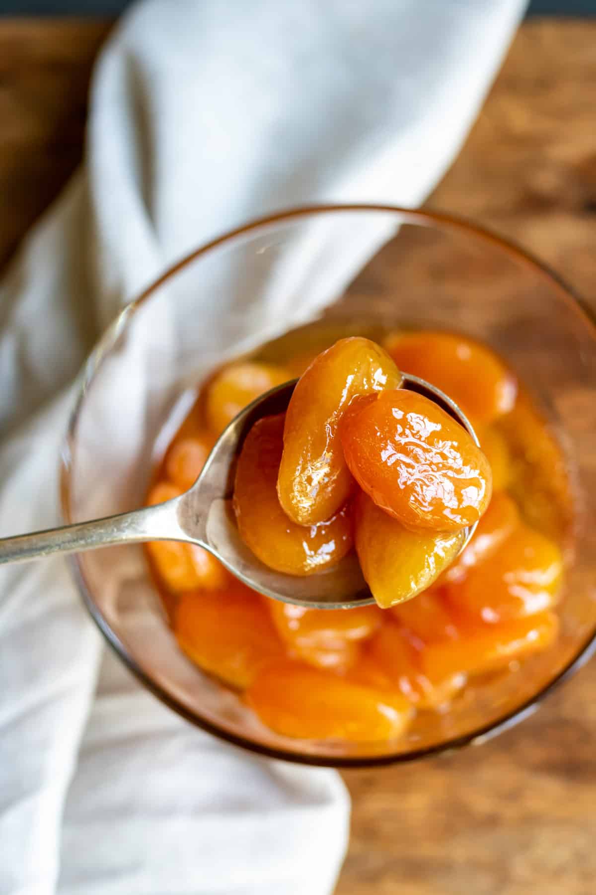 Spoonful of glazed apricots coming out of a bowlful.