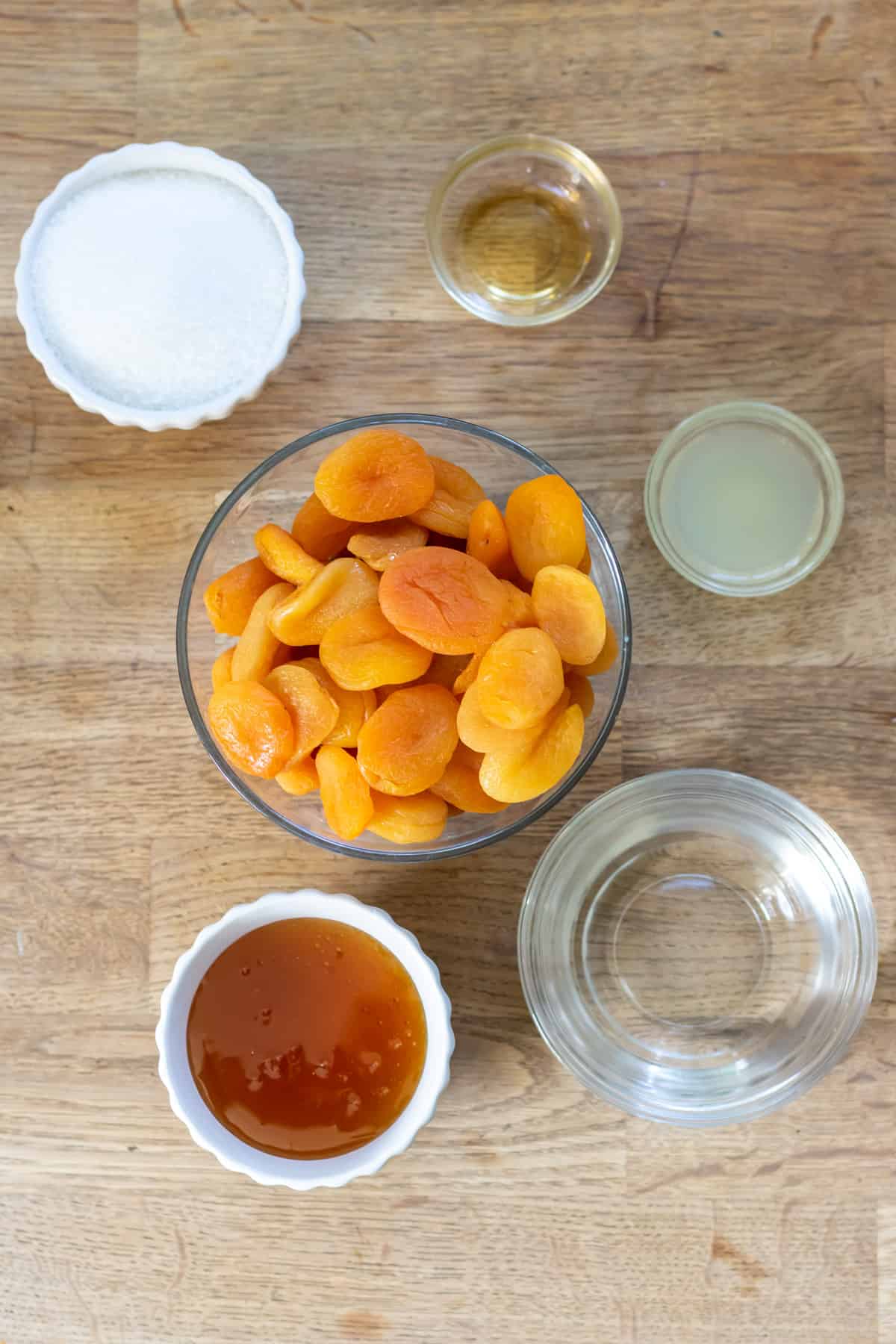 Apricots, sugar, water, honey, lemon juice and vanilla on a table.