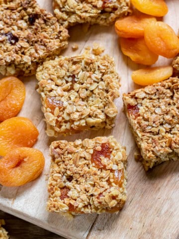 Slices of apricot flapjacks on a wooden board, next to dried apricots.