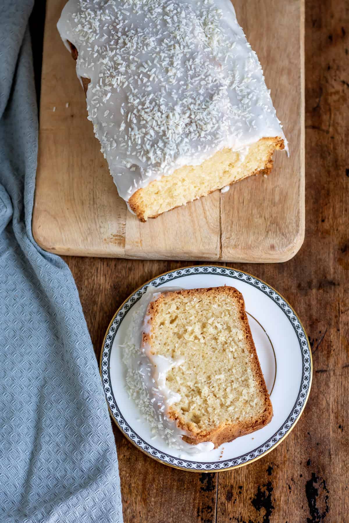 Looking down at a wooden table with a coconut loaf cake and a slice on a plate.