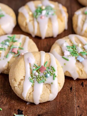 Pile of condensed milk cookies with icing and sprinkles, on a wooden table.