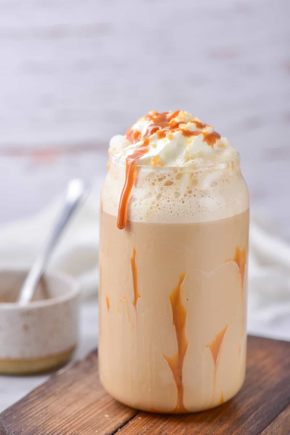 Side view of a glass with caramel sauce around the inside, frappuccino, whipped cream and crushed caramel candies.