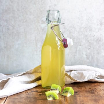 Glass bottle of kiwi simple syrup on a wooden table.