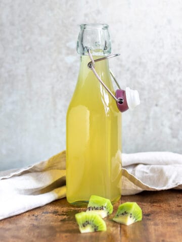 Glass bottle of kiwi simple syrup on a wooden table.