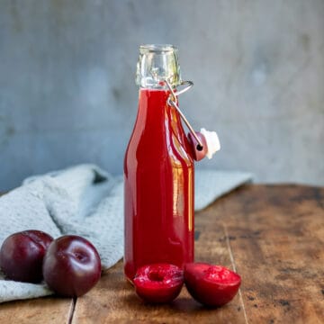 Plum simple syrup in a bottle on a wooden table.