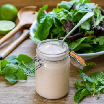 Spoon in a jar of salsa ranch dressing, in front of a bowl of salad.