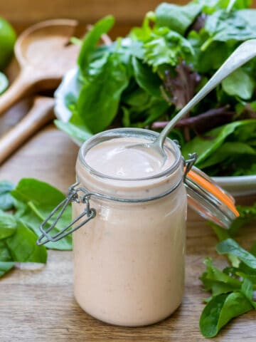 Spoon in a jar of salsa ranch dressing, in front of a bowl of salad.