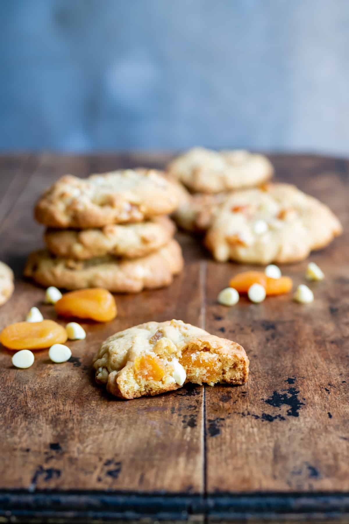 An apricot cookie with a bite out in front of more cookies, on a wooden table.