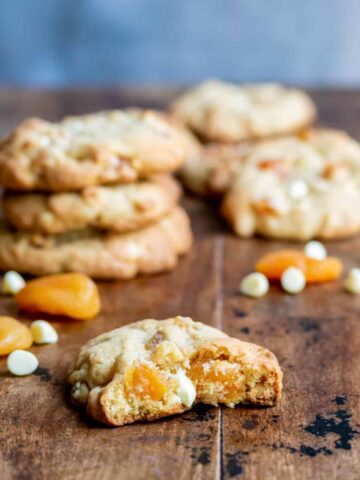 An apricot cookie with a bite out in front of more cookies, on a wooden table.