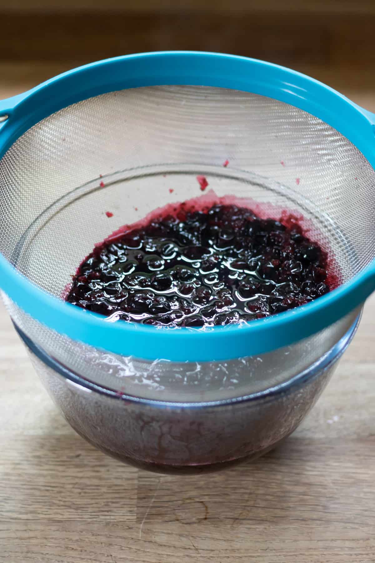 Straining the blackcurrant syrup into a bowl.