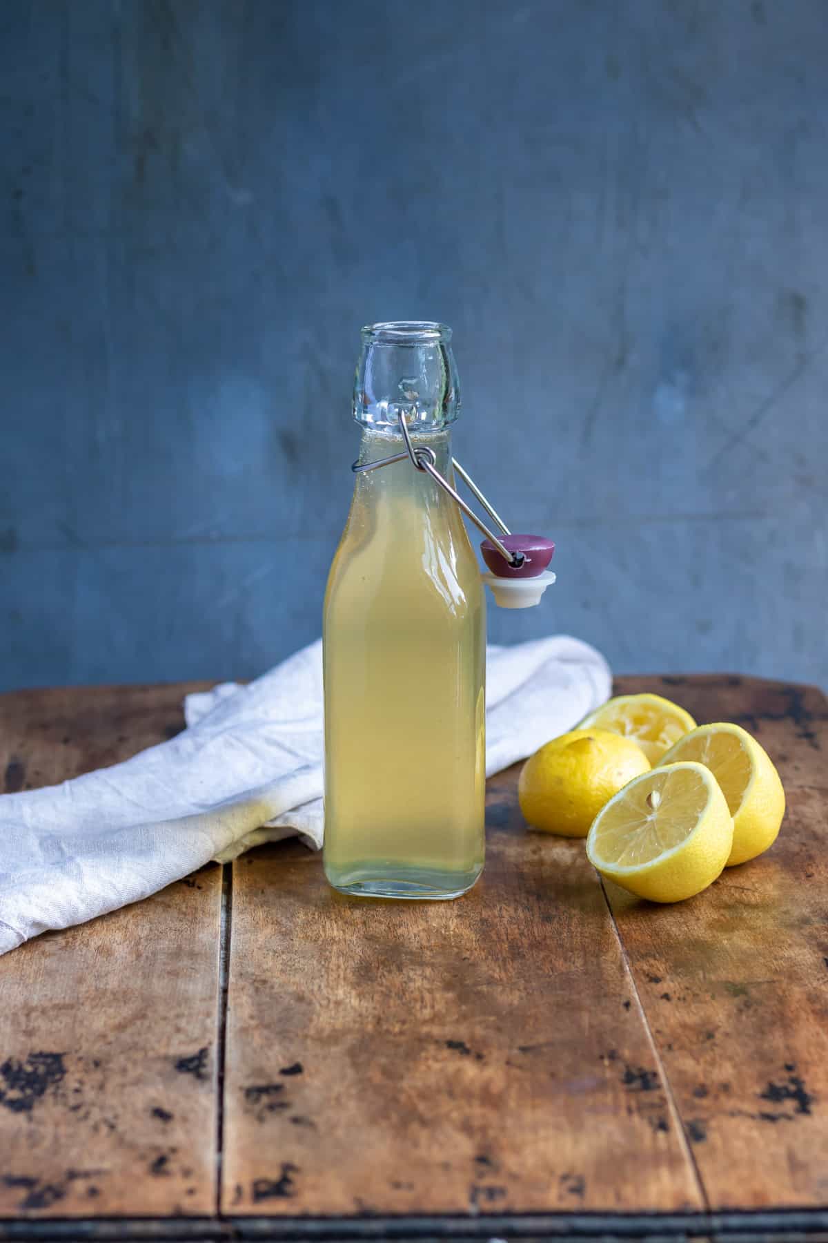 Bottle of lemon syrup and cut lemons on a table.