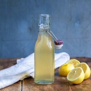 Close up of a bottle of lemon simple syrup on a wooden table, next to cut lemons.