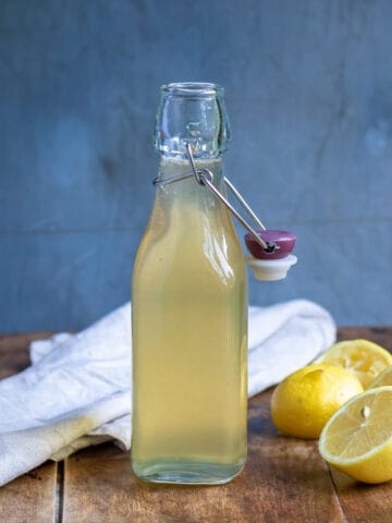 Close up of a bottle of lemon simple syrup on a wooden table, next to cut lemons.