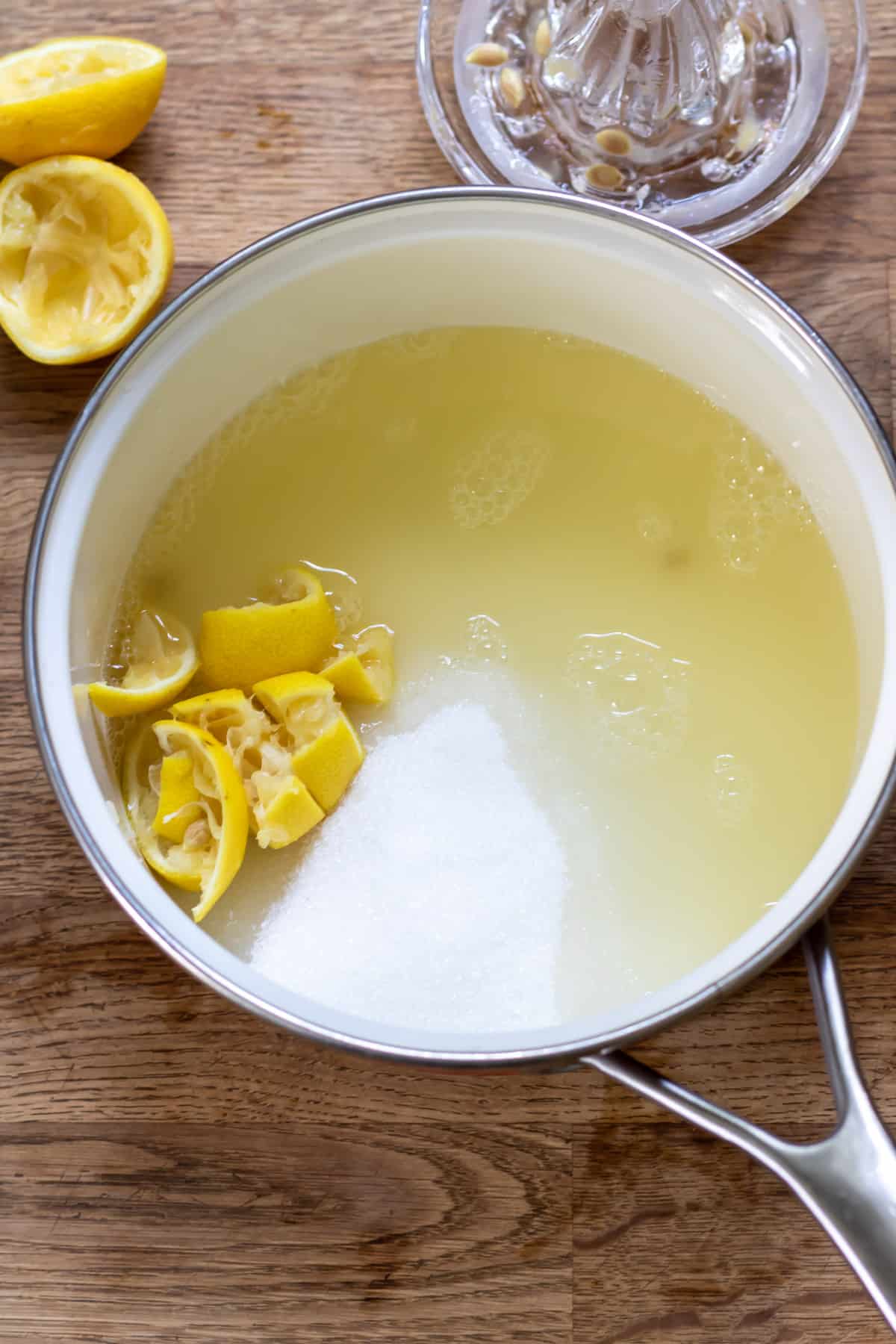 Lemons and lemon juice being added to a pot of sugar and water.
