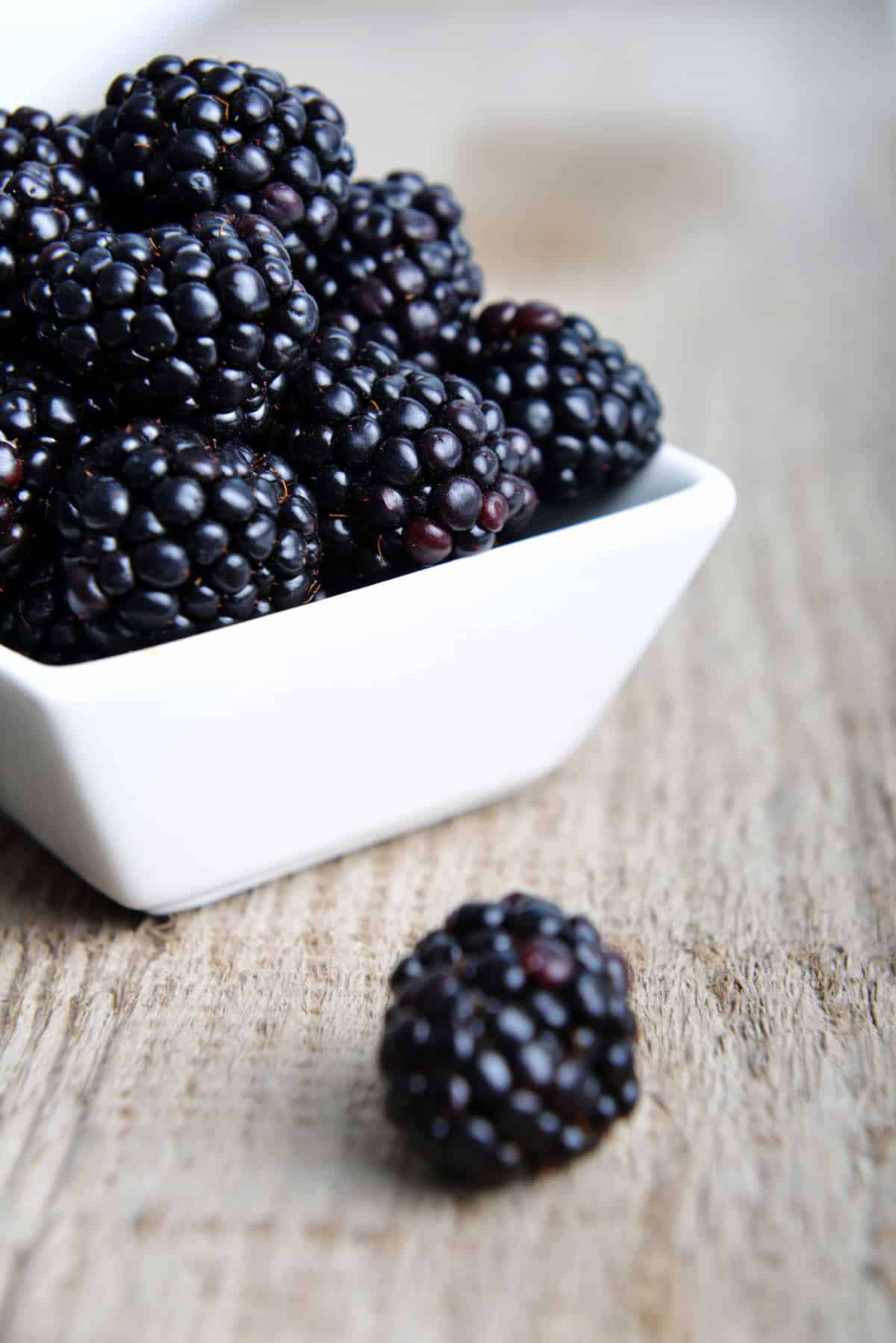 Bowl of fresh blackberries on a wooden table.