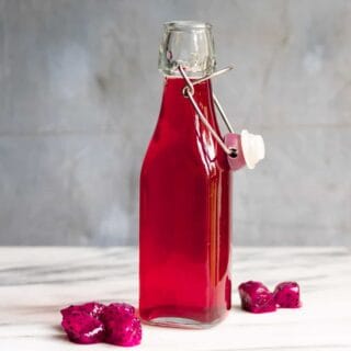 Glass bottle of dragon fruit syrup next to pieces of pitaya.