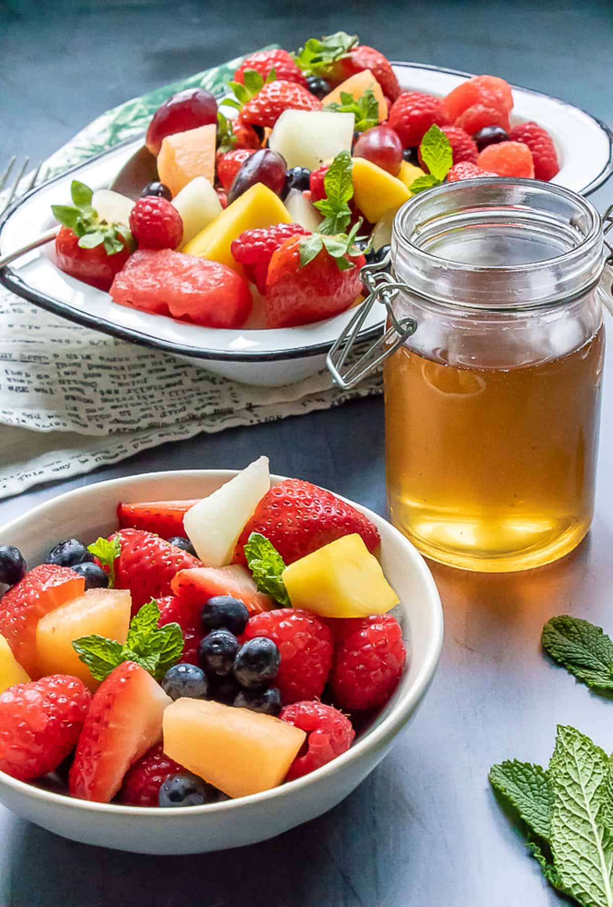 Fruit salad in dishes, next to a jar of tea syrup.