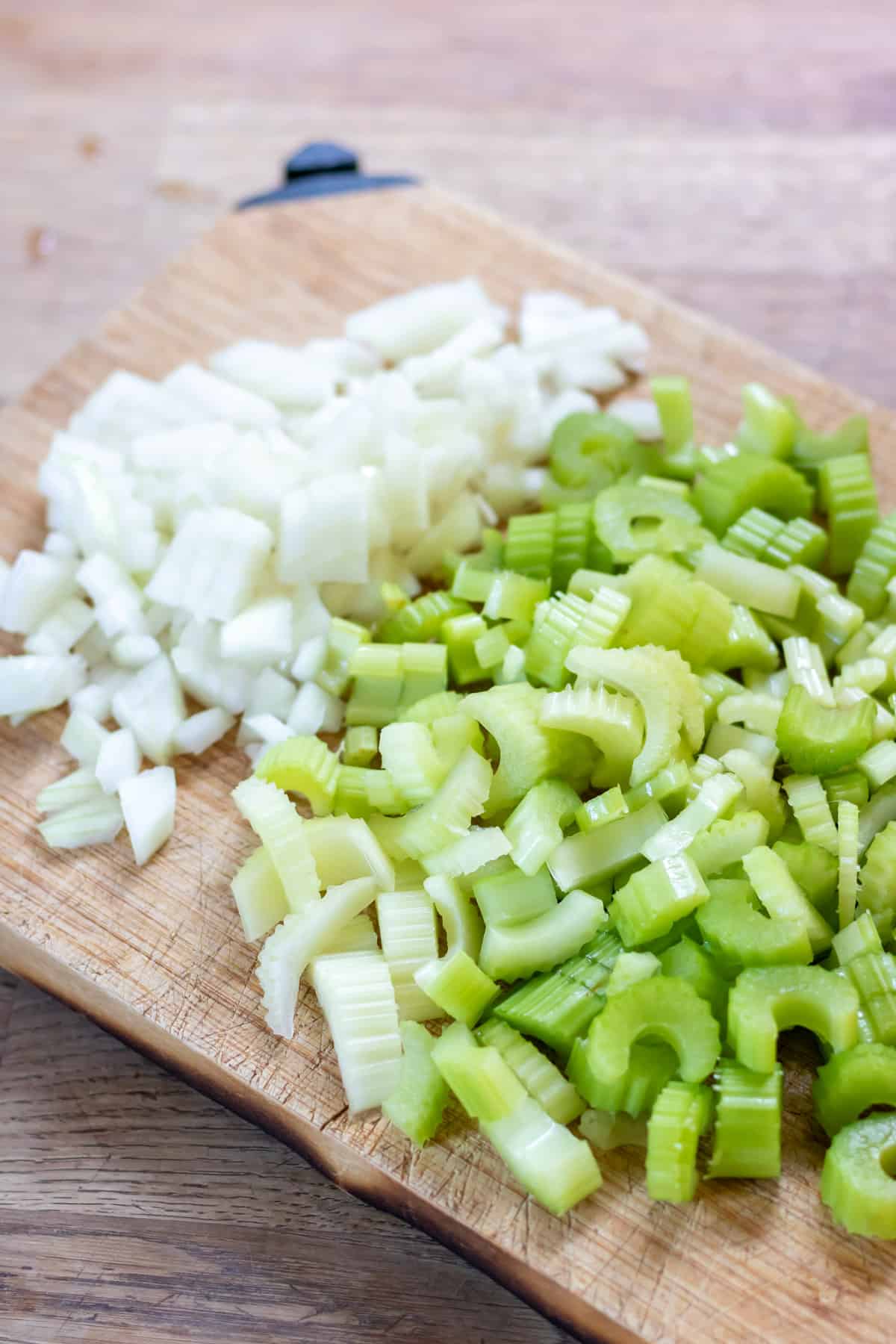 Chopped onion and celery on a wooden board.