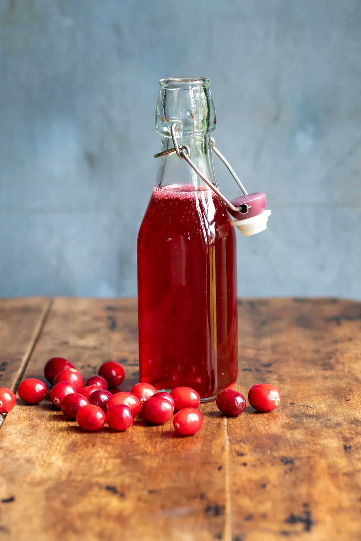 Bottle of cranberry syrup on a wooden table next to fresh cranberries.